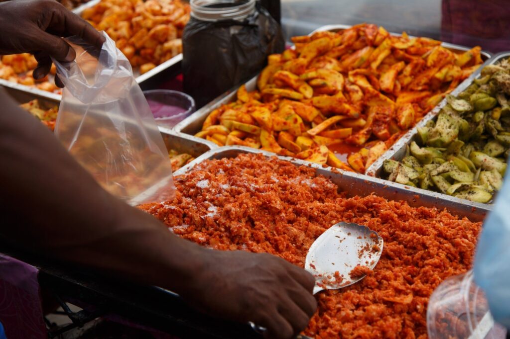 A close-up of a street food stall selling a variety of pickled fruits, including mango and ambarella. Experiencing local cuisine and street food is a popular cultural activity offered by the best Tour Operators in Sri Lanka and a professional Tour Company in Sri Lanka.