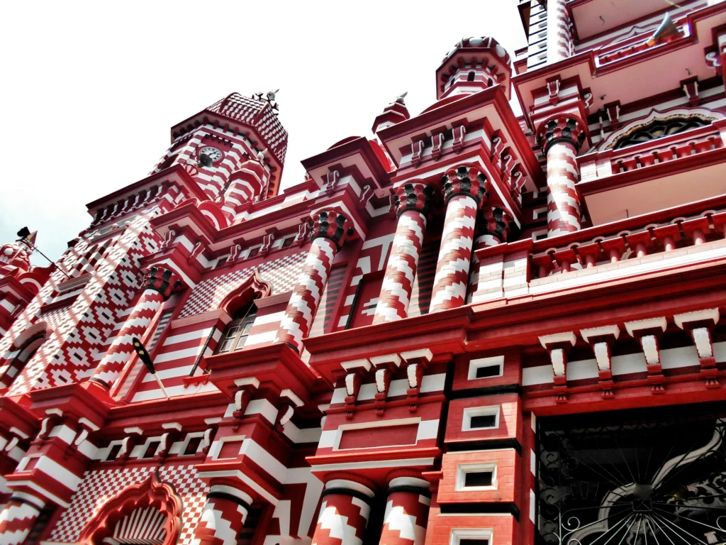 A striking low-angle shot of the Jami Ul-Alfar Mosque in Colombo, showcasing its distinctive red and white striped patterns. This iconic landmark is a highlight of city tours organized by expert Tour Operators in Sri Lanka and a must-see site for travelers with a professional Tour Company in Sri Lanka.