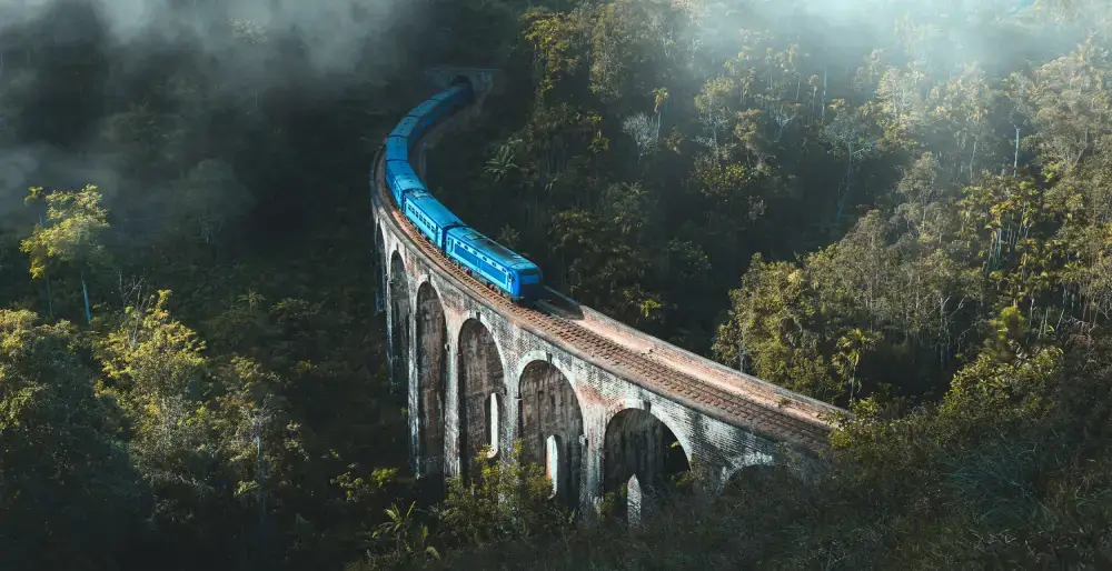A blue train travels across the iconic Nine Arch Bridge in Ella, a stunning engineering marvel in the misty mountains of Sri Lanka, a highlight of tours provided by top Tour Operators in Sri Lanka and a professional Tour Company in Sri Lanka.