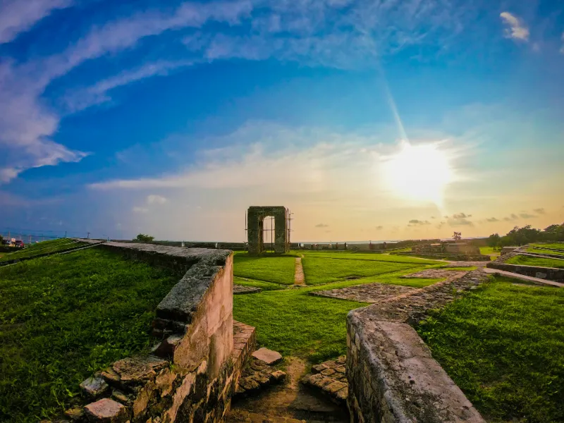 A historic fort's grassy courtyard and stone walls are illuminated by the setting sun, creating a dramatic and beautiful scene. Experiencing cultural sites like this is a key part of tours with Ceylon Roots, a leading Tour Company in Sri Lanka.