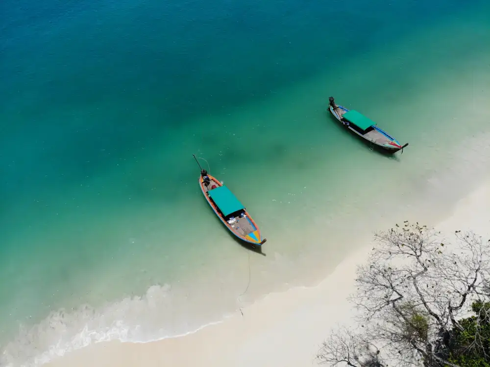 An aerial view of two boats in stunning turquoise water near a white sand beach, representing the beautiful beach holidays and excursions offered by a leading Tour Operators in Sri Lanka and Tour Company in Sri Lanka.